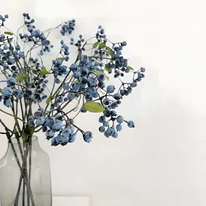 Five artificial blueberry branches neatly arranged in a clear glass vase, forming an elegant floral arrangement. The rich, lifelike blueberry fruits and delicate green leaves create a fresh and natural look, ideal for home décor, event styling, or office settings.