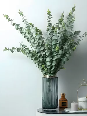 The artificial green eucalyptus stem arranged in a transparent glass vase. The minimalist design adds a touch of elegance to any interior setting, enhancing modern or rustic decor styles.