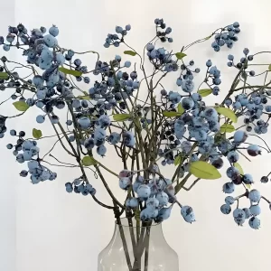 This close-up image highlights the realistic details of the artificial blueberry floral arrangement. The blueberries are plump and vibrant, with lifelike texture, while the green leaves feature intricate vein patterns, adding depth and authenticity. This finely crafted piece makes for a stunning and durable decorative accent.