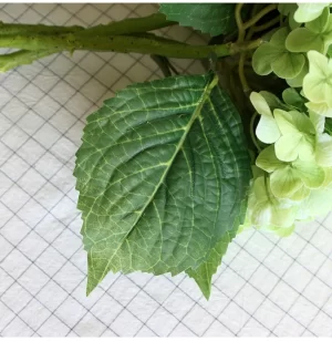 A detailed close-up of the artificial hydrangea's green leaf, highlighting the realistic texture and visible veins, providing an authentic touch to the overall appearance of the plant.