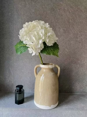 A single stem of white artificial hydrangea beautifully displayed in a cream-colored ceramic vase, adding a simple yet elegant touch to any decor with its lifelike petals and natural form.