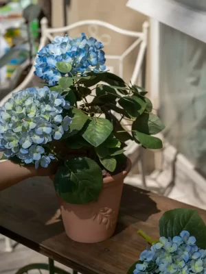 This large faux blue hydrangea arrangement is placed on a rustic outdoor bench, bringing vibrant colors and a natural aesthetic to any garden or patio space.