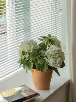 This large artificial white hydrangea is placed on a sunny windowsill alongside books, creating a serene and literary atmosphere. The simplicity of the arrangement brings a sense of calm and warmth to any room.