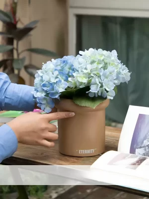 This small faux blue hydrangea arrangement sits beside books on an outdoor flower basket, offering a calm and peaceful vibe. The deep blue flowers bring a pop of color to your outdoor relaxation space.