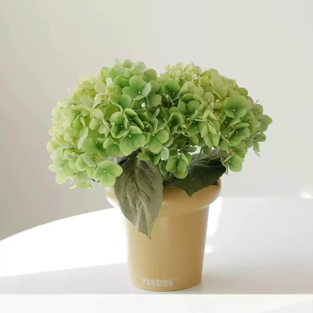 Bring nature indoors with this small faux green hydrangea in a cream-colored pot. The soft green tones create a serene and natural atmosphere, making it a versatile addition to your home decor.