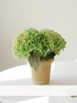 Bring nature indoors with this small faux green hydrangea in a cream-colored pot. The soft green tones create a serene and natural atmosphere, making it a versatile addition to your home decor.