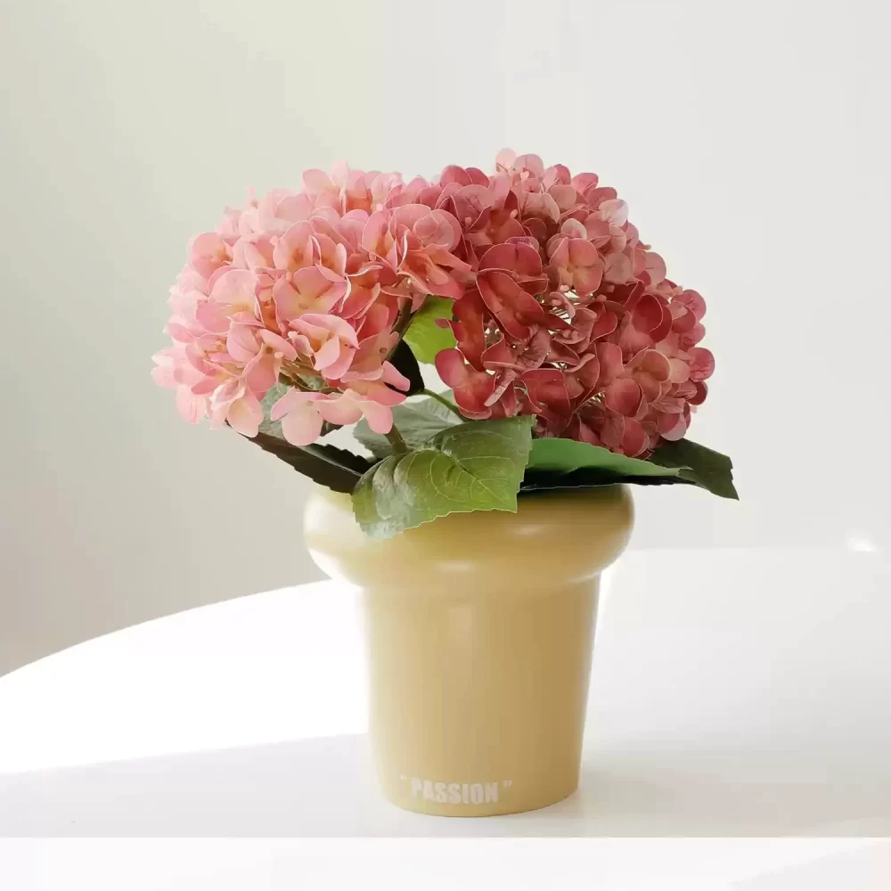 This small potted artificial hydrangea in vibrant pink adds a cheerful touch to any interior. The cream pot enhances the softness of the pink blossoms, creating a beautiful contrast.