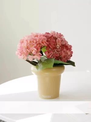 This small potted artificial hydrangea in vibrant pink adds a cheerful touch to any interior. The cream pot enhances the softness of the pink blossoms, creating a beautiful contrast.