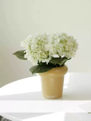 A minimalist display, this small artificial hydrangea arrangement includes two white stems in a stylish cream-colored pot. Ideal for brightening up any room with a touch of subtle elegance and sophistication.