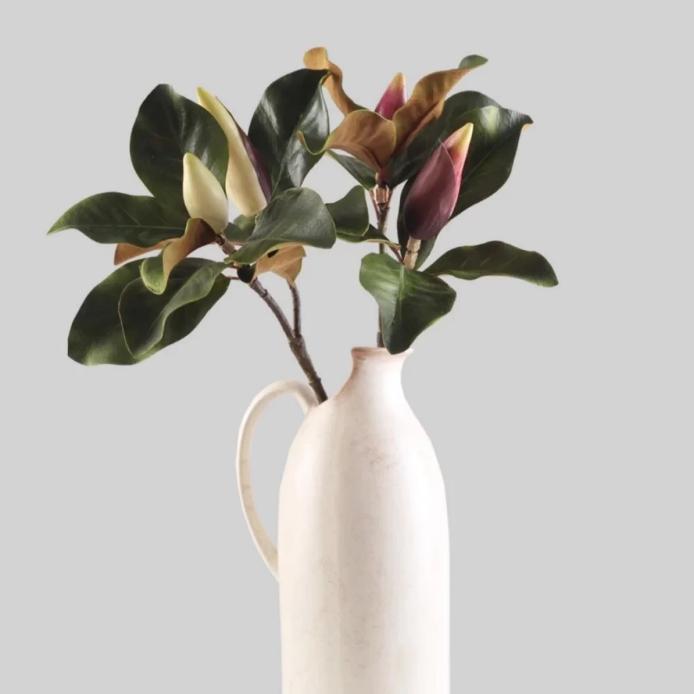 This striking floral arrangement pairs white and burgundy magnolia buds in a beautifully designed ceramic vase. The combination of the vibrant flower colors with the classic vase creates a stunning display that enhances any interior, perfect for living rooms, dining areas, or as a centerpiece for special occasions.