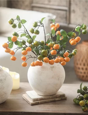 Displaying an arrangement of green and yellow kumquat stems, this ceramic vase stands out with its earthy texture and full-bodied shape. The bright colors of the faux kumquats beautifully complement the vase’s understated design, adding a fresh and vibrant touch to your decor.