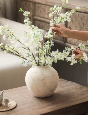 The vase elegantly holds faux white snow willow branches, enhancing its vintage charm. The branches’ subtle white hues harmonize with the vase’s creamy tones, creating a serene and refined look ideal for any decor style, from rustic to minimalist.