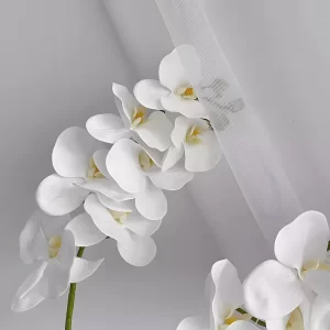 A close-up shot highlighting the exquisite details of a single artificial white orchid stem, featuring seven blooms. Each petal is meticulously crafted to mimic the natural texture and beauty of real orchids.