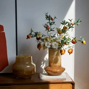 This arrangement pairs the amber cone-shaped and round vases filled with faux flowers, bathed in soft sunlight, creating a beautiful and welcoming focal point on any surface.