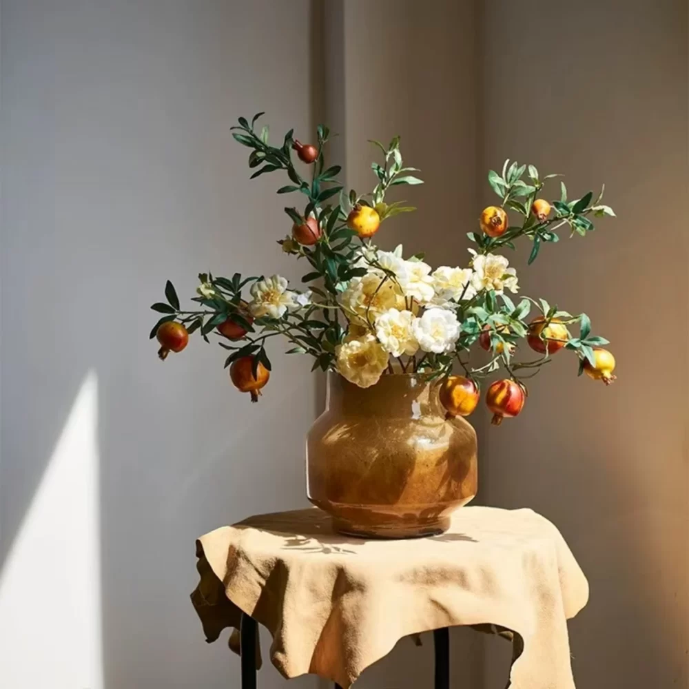 The round amber vase is filled with faux pomegranates, creating a vivid and colorful arrangement that's perfect for adding a natural, harvest-inspired touch to your home.