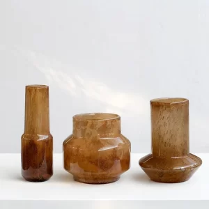 A set of three hand-blown amber glass vases, each with a distinct shape and size. This collection brings a sense of harmony and variety to any space.