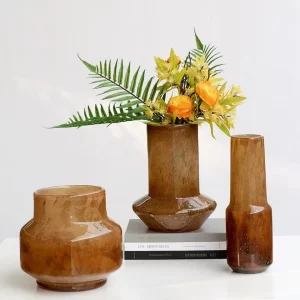 The set of three amber vases includes a centerpiece filled with yellow faux flowers, creating a simple yet eye-catching display suitable for any home setting.