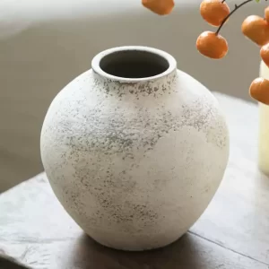 A beautiful, rounded ceramic vase crafted in rustic, wabi-sabi style. This sturdy piece stands 8.7 inches tall with a mouth diameter of 3.1 inches and a max diameter of 8.7 inches. The textured surface and subtle white tones give it an authentic vintage appeal, perfect for enhancing any room’s aesthetic.